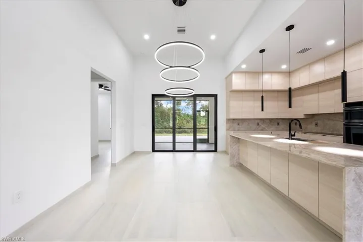 Kitchen with light stone counters, dobule oven black, a sink, backsplash, and modern cabinets