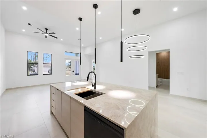 Kitchen featuring dishwashing machine, modern cabinets, light stone counters, open floor plan, and a sink