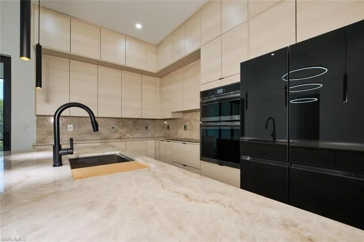 Kitchen with decorative backsplash, a sink, light stone countertops, and double wall oven