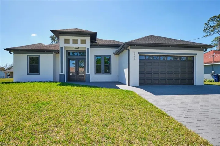 Prairie-style house with a front yard, french doors, stucco siding, an attached garage, and decorative driveway