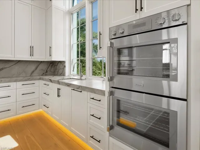 Kitchen featuring stainless steel double oven, white cabinetry, healthy amount of natural light, and light stone counters