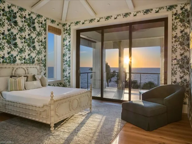 Bedroom with beam ceiling, wallpapered walls, wood finished floors, a water view, and access to exterior