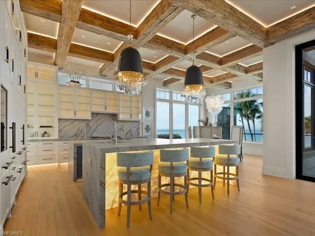 Kitchen featuring a breakfast bar, hanging light fixtures, light stone countertops, beam ceiling, and coffered ceiling