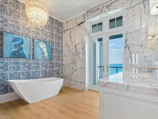 Bathroom with tile walls, wood finished floors, a chandelier, a freestanding bath, and a water view