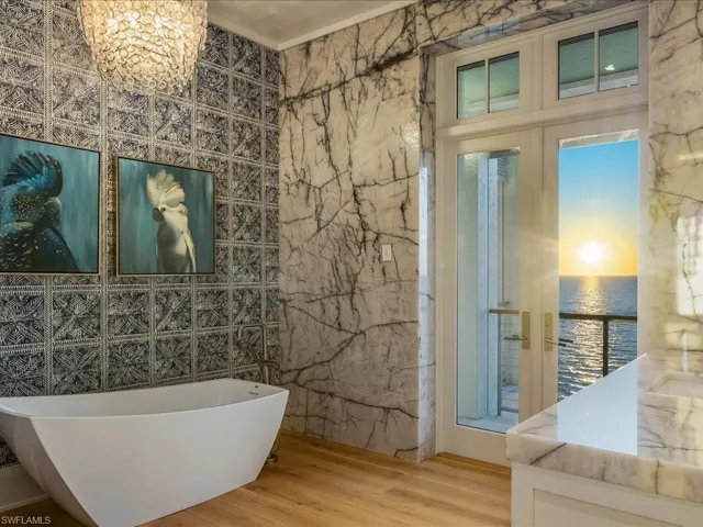 Full bathroom with a freestanding tub, tile walls, a water view, wood finished floors, and a chandelier