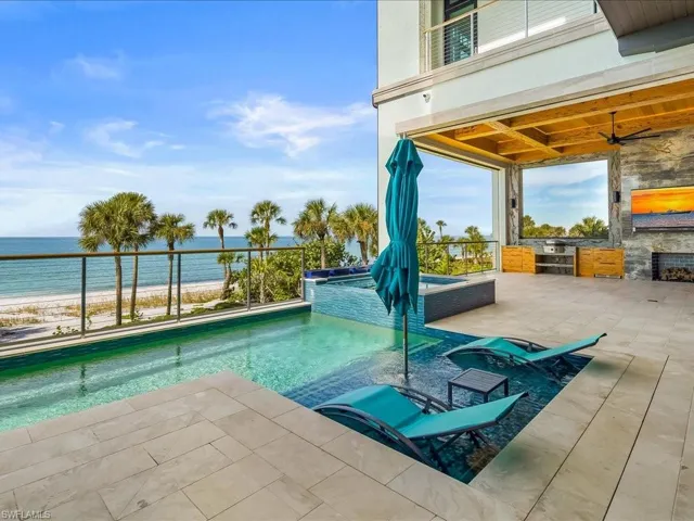 View of pool with view of water and beach, a pool with connected hot tub, a patio area, and an outdoor kitchen