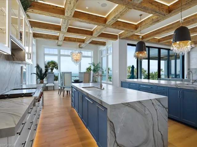 Kitchen featuring blue cabinets, a large island with sink, decorative light fixtures, light stone countertops, and a chandelier