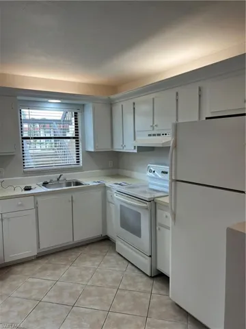 Kitchen featuring fridge, range, light countertops, light tile patterned flooring, and extractor fan