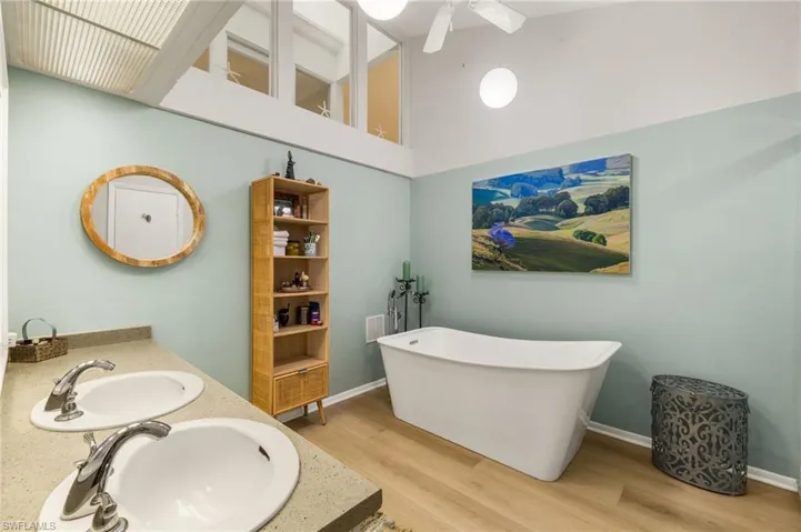 Bathroom with double vanity, wood finished floors, a soaking tub, and a sink