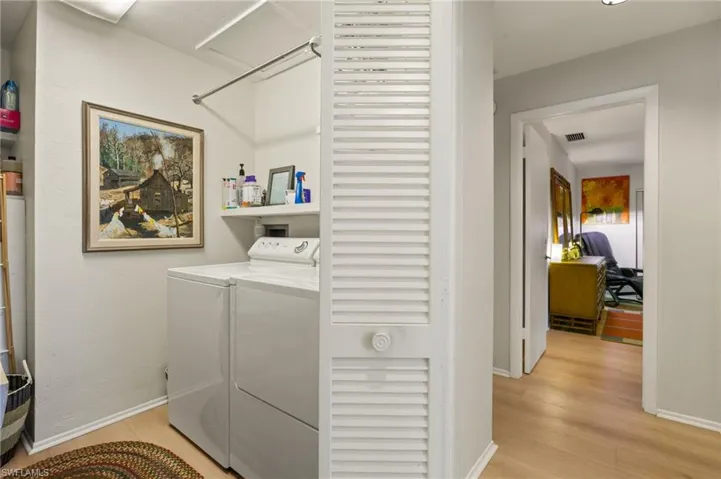 Washroom featuring washer and clothes dryer, visible vents, light wood-style flooring, and baseboards