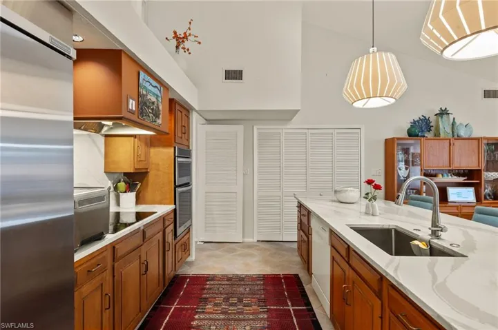 Kitchen with a sink, visible vents, appliances with stainless steel finishes, brown cabinetry, and decorative light fixtures