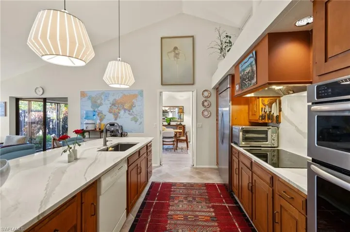Kitchen with appliances with stainless steel finishes, brown cabinets, a sink, and decorative light fixtures