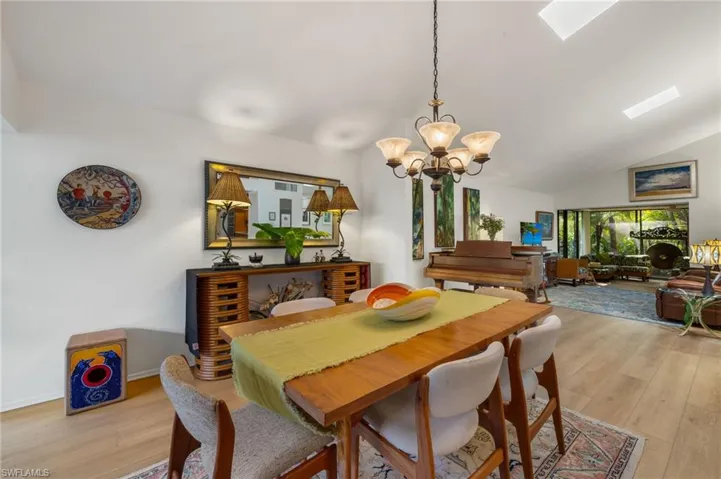 Dining space featuring vaulted ceiling with skylight, light wood-style flooring, a chandelier, and baseboards