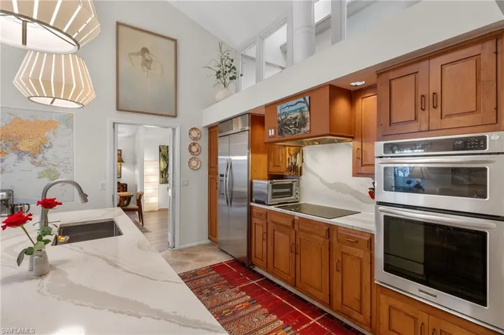 Kitchen featuring appliances with stainless steel finishes, brown cabinets, decorative light fixtures, and a sink