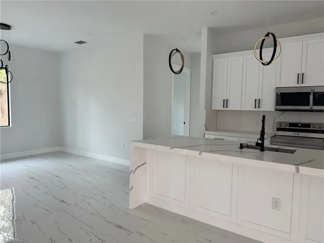 Kitchen with decorative light fixtures, light stone counters, white cabinetry, and appliances with stainless steel finishes