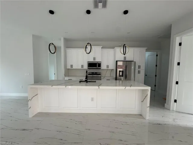 Kitchen with pendant lighting, white cabinets, a spacious island, light stone countertops, and appliances with stainless steel finishes