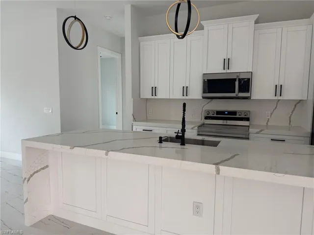 Kitchen featuring light stone countertops, stainless steel appliances, sink, pendant lighting, and white cabinets