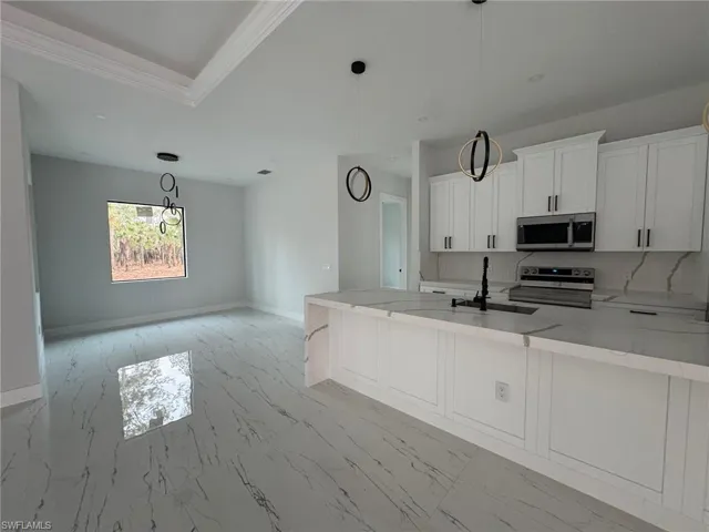 Kitchen featuring white cabinets, sink, hanging light fixtures, light stone countertops, and stainless steel appliances