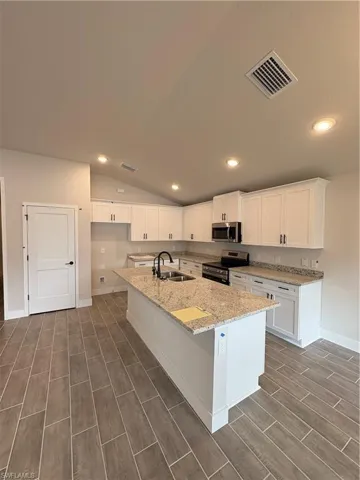 Kitchen featuring lofted ceiling, light stone counters, stove, white cabinets, and recessed lighting