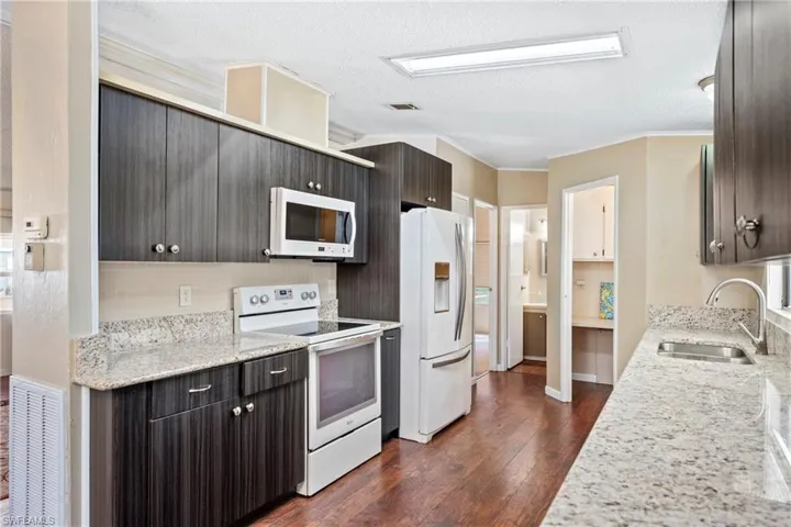 Updated Kitchen with white appliances, light stone counters, crown molding, dark wood finished floors, and dark brown cabinets