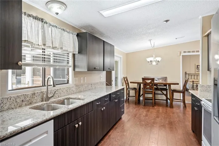 Updated Kitchen featuring light stone counters, pendant lighting, dark wood-style floors, a chandelier, and a textured ceiling