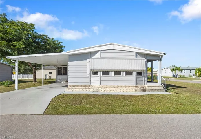 Manufactured / mobile home featuring a front yard, driveway, and a carport