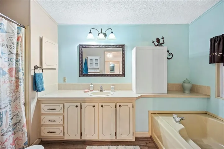 Bathroom featuring vanity, a textured ceiling, a bath, a shower with curtain, and dark wood finished floors
