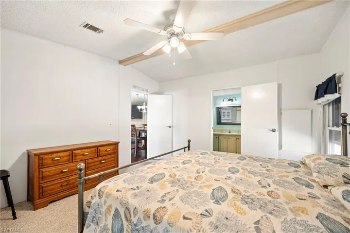 Bedroom with light carpet, a textured ceiling, a ceiling fan, ensuite bath, and lofted ceiling