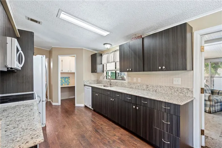 Updated Kitchen featuring tasteful backsplash, light stone counters, white appliances, ornamental molding, and dark wood-type flooring