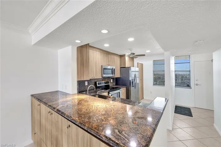 Kitchen featuring dark stone counters, stainless steel appliances, a textured ceiling, decorative backsplash, and recessed lighting