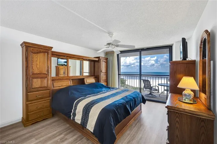 Primary Bedroom with a textured ceiling, wood finished floors, access to exterior, expansive windows, and ceiling fan