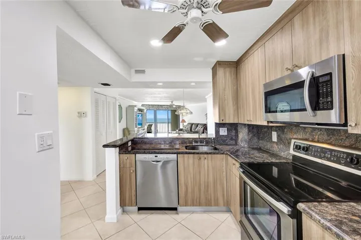 Kitchen with stainless steel appliances, a peninsula, light tile patterned flooring, ceiling fan, and dark stone counters