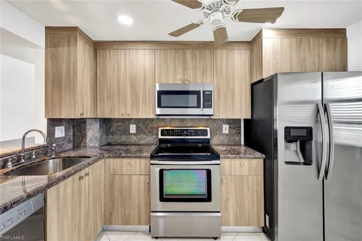 Kitchen with stainless steel appliances, dark stone counters, light brown cabinetry, and tasteful backsplash