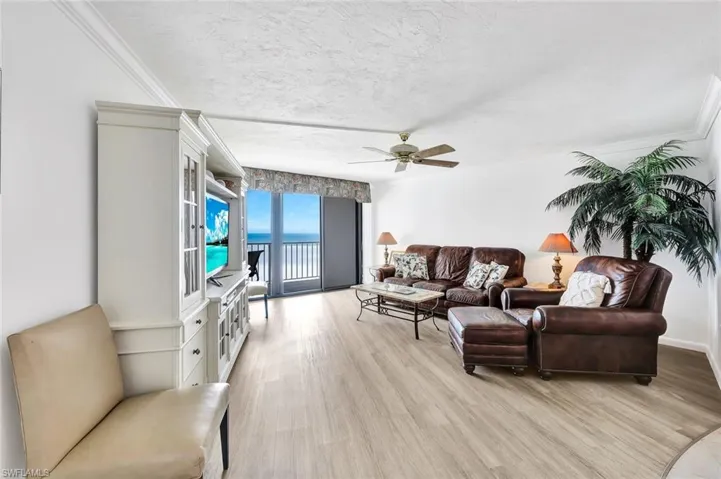 Living room with ceiling fan, crown molding, light wood-style flooring, and a textured ceiling