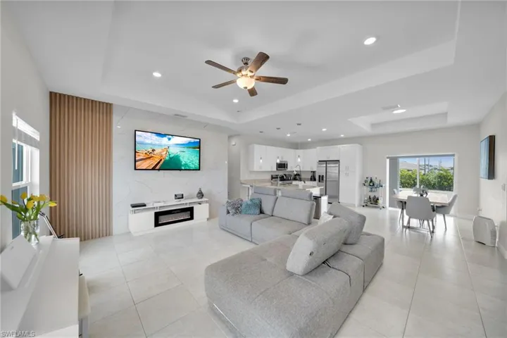 Living room with a raised ceiling, ceiling fan, recessed lighting, light tile patterned floors, and a glass covered fireplace