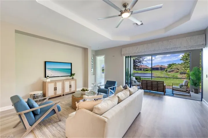Living room featuring light wood-type flooring, a raised ceiling, and ceiling fan