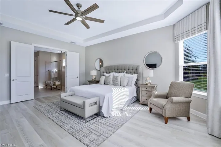 Bedroom featuring multiple windows, a raised ceiling, light wood-type flooring, and ceiling fan