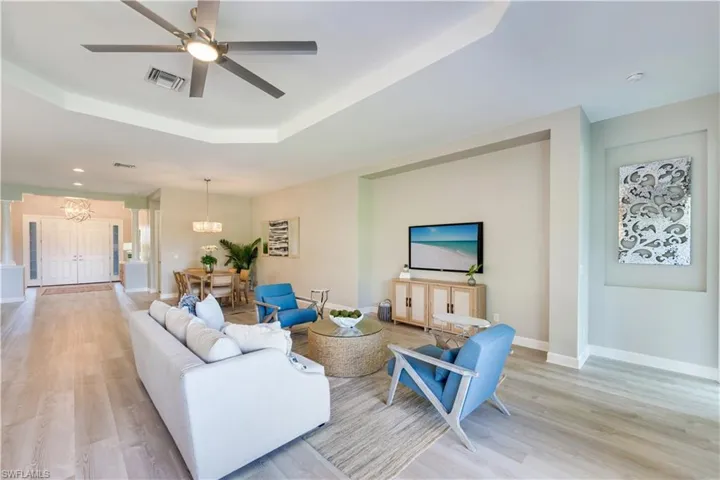 Living room featuring ceiling fan with notable chandelier, light wood-type flooring, and a raised ceiling