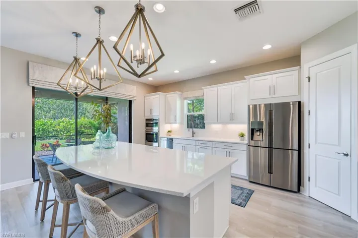 Kitchen with light hardwood / wood-style floors, a notable chandelier, white cabinets, hanging light fixtures, and appliances with stainless steel finishes