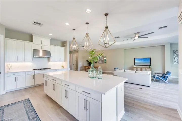 Kitchen with hanging light fixtures, white cabinetry, ceiling fan with notable chandelier, a center island, and light hardwood / wood-style flooring