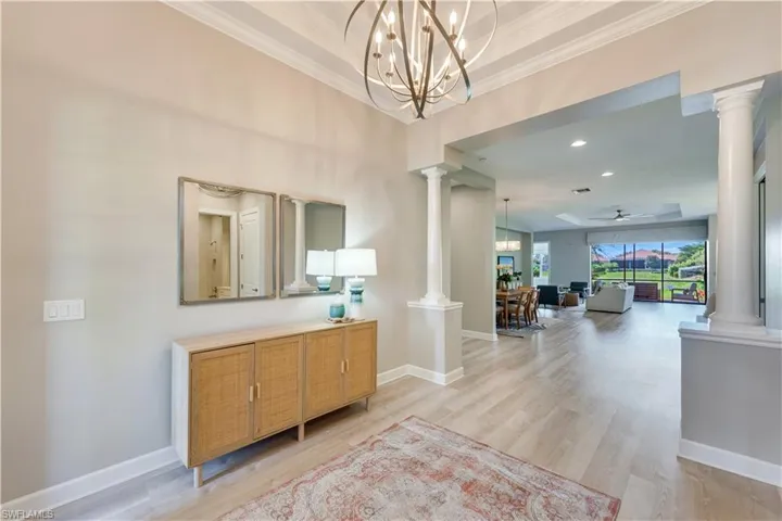 Hall featuring a notable chandelier, light hardwood / wood-style flooring, crown molding, and ornate columns