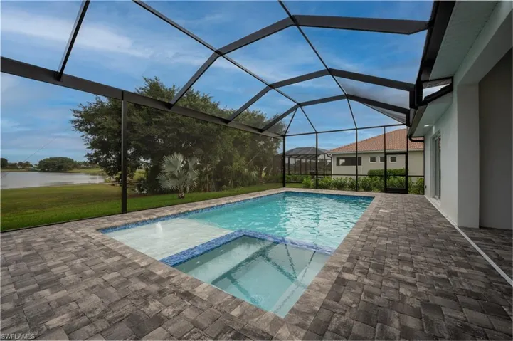 View of swimming pool with a sunroom, a patio area, a pool with connected hot tub, a water view, and a lawn