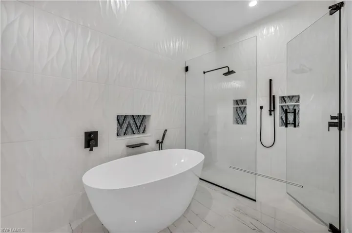 Bathroom featuring walk in shower, a freestanding bath, tile walls, marble finish flooring, and recessed lighting