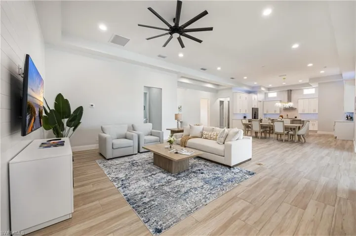 Living area with light wood-style floors, recessed lighting, ceiling fan, and a raised ceiling