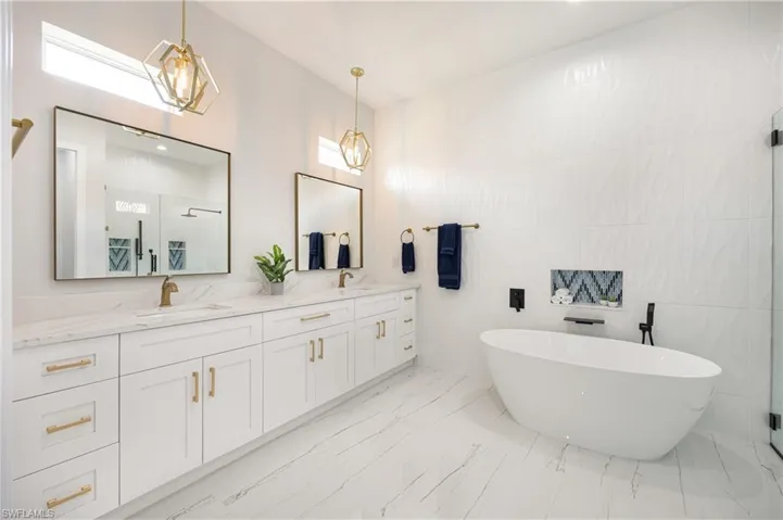 Full bathroom with a shower stall, double vanity, a freestanding tub, tile walls, and light marble finish floors