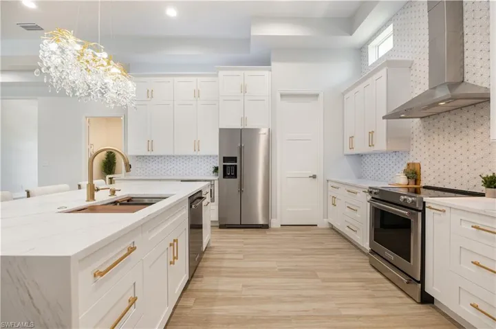 Kitchen with wall chimney exhaust hood, stainless steel appliances, white cabinets, and light stone counters