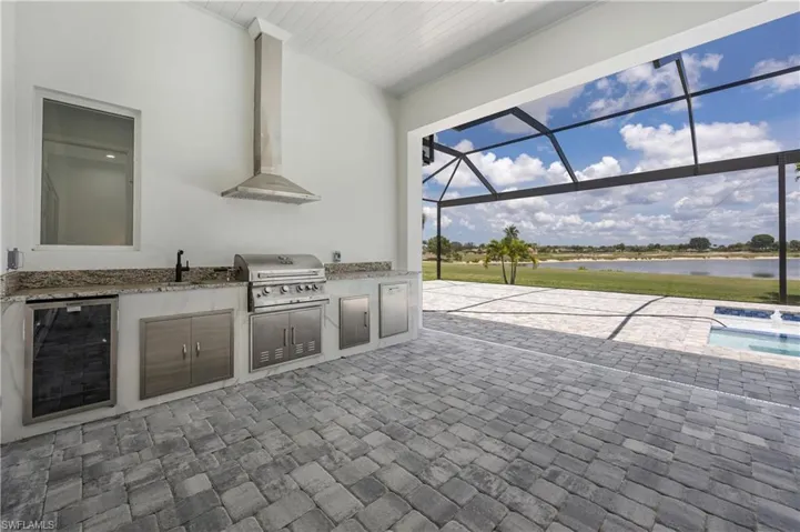 View of patio featuring a sunroom, a lanai, a water view, exterior kitchen, and beverage cooler