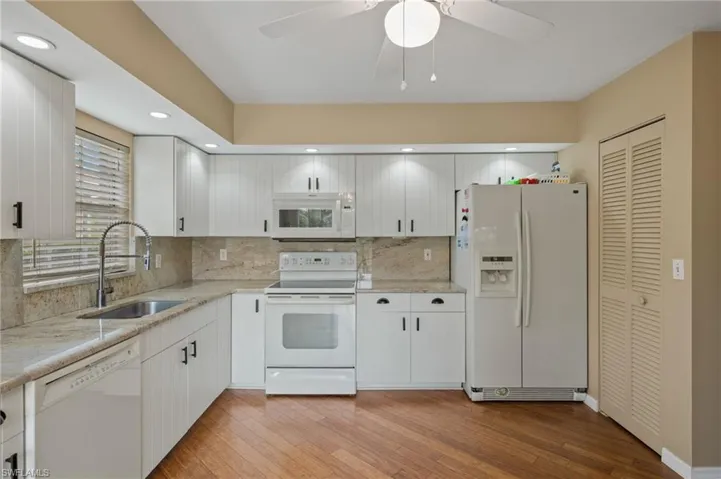 Kitchen with white appliances, sink, ceiling fan, decorative backsplash, and light hardwood / wood-style floors