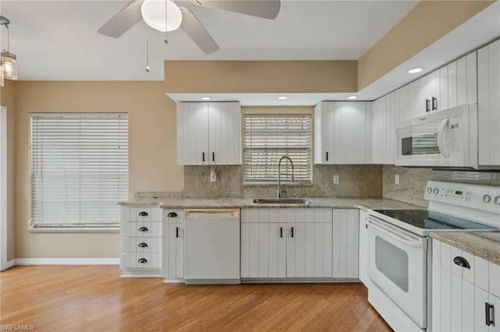 Kitchen featuring white appliances, light hardwood / wood-style floors, sink, decorative backsplash, and white cabinetry