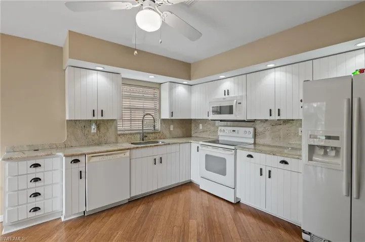 Kitchen featuring white appliances, sink, decorative backsplash, ceiling fan, and light hardwood / wood-style floors